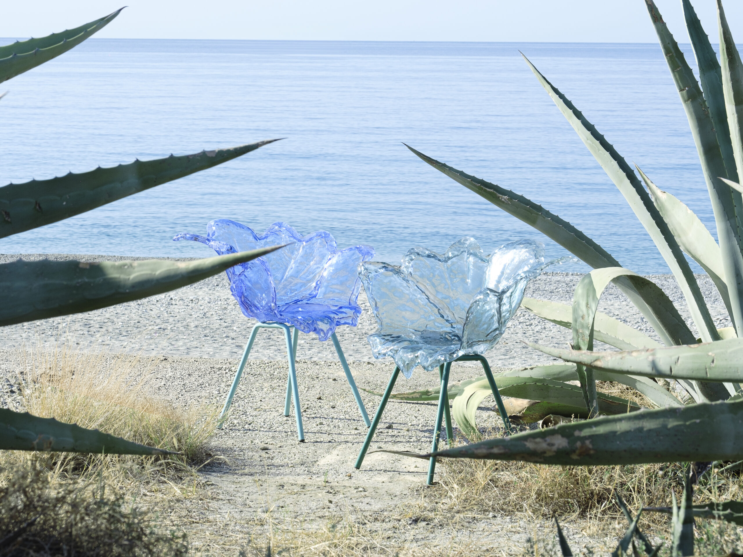 Chaises Agave Sturm Milano aux coques transparentes bleutées, photographiées face à la mer